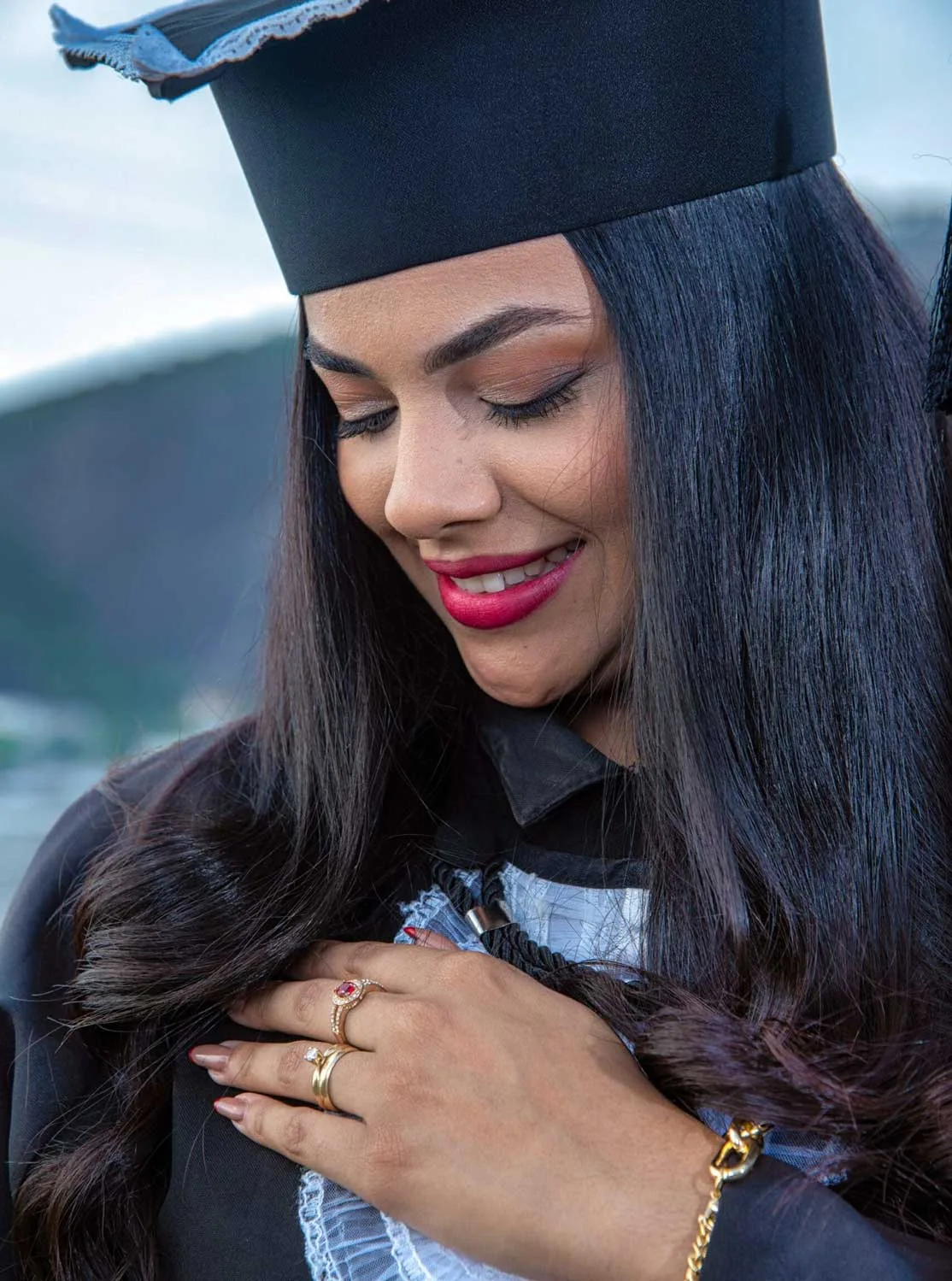 Formanda de beca sorri com a mão no peito em ensaio de formatura no Aterro do Flamengo