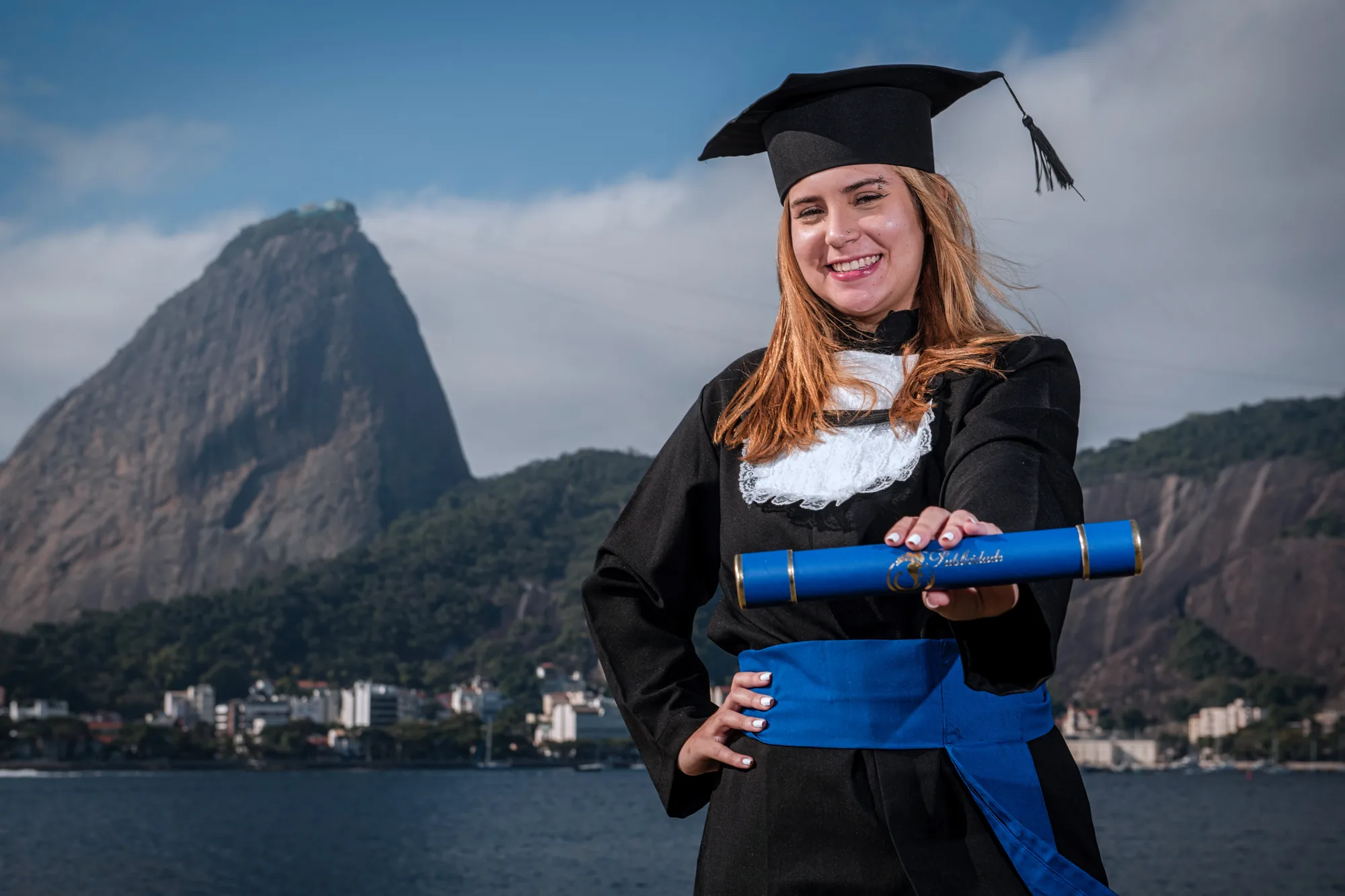 Formanda de beca mostra o canudo azul diante do Pão de Açúcar