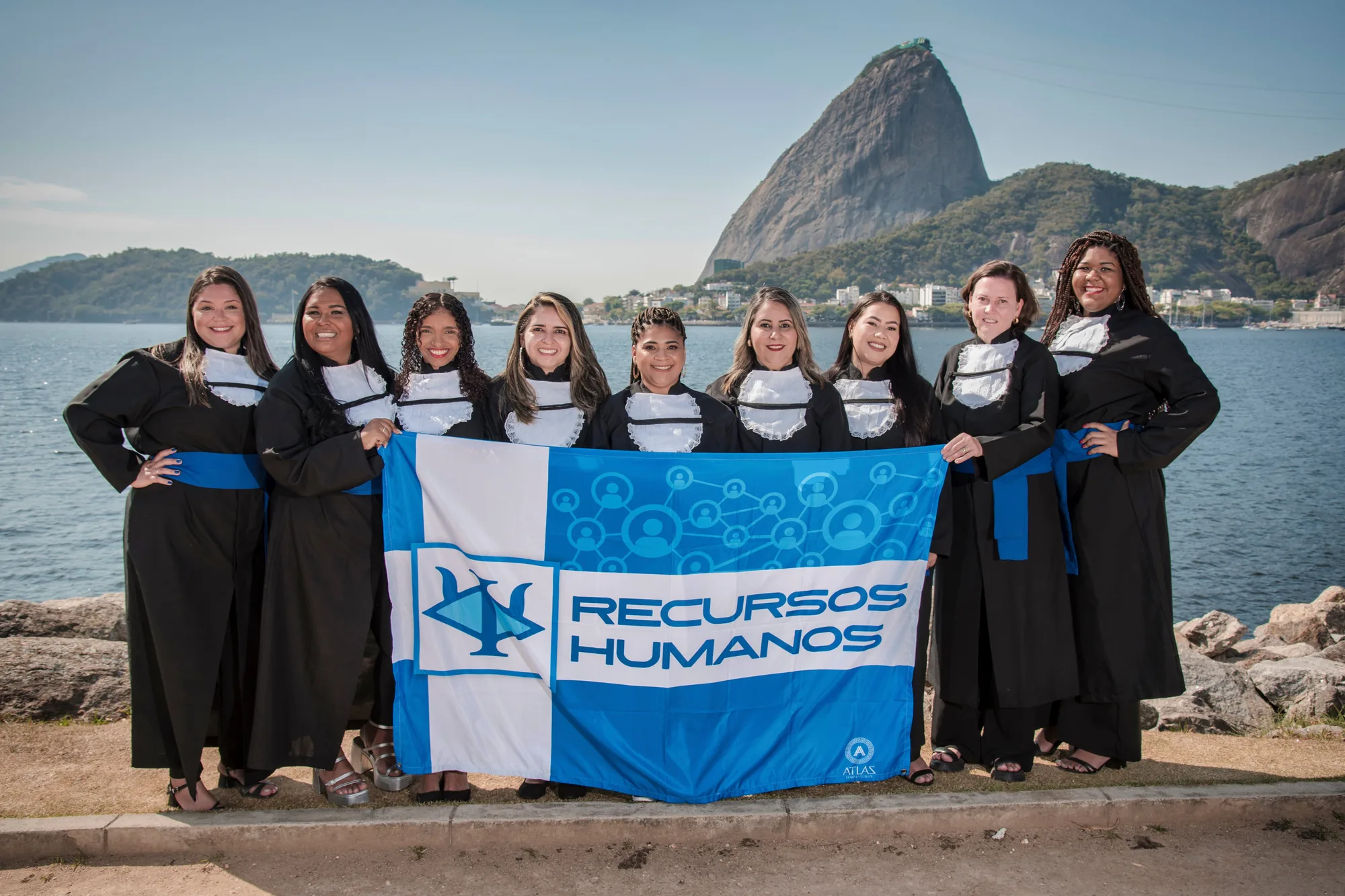 Turma de Recursos Humanos segura a bandeira do curso, com o Pão de Açúcar ao fundo