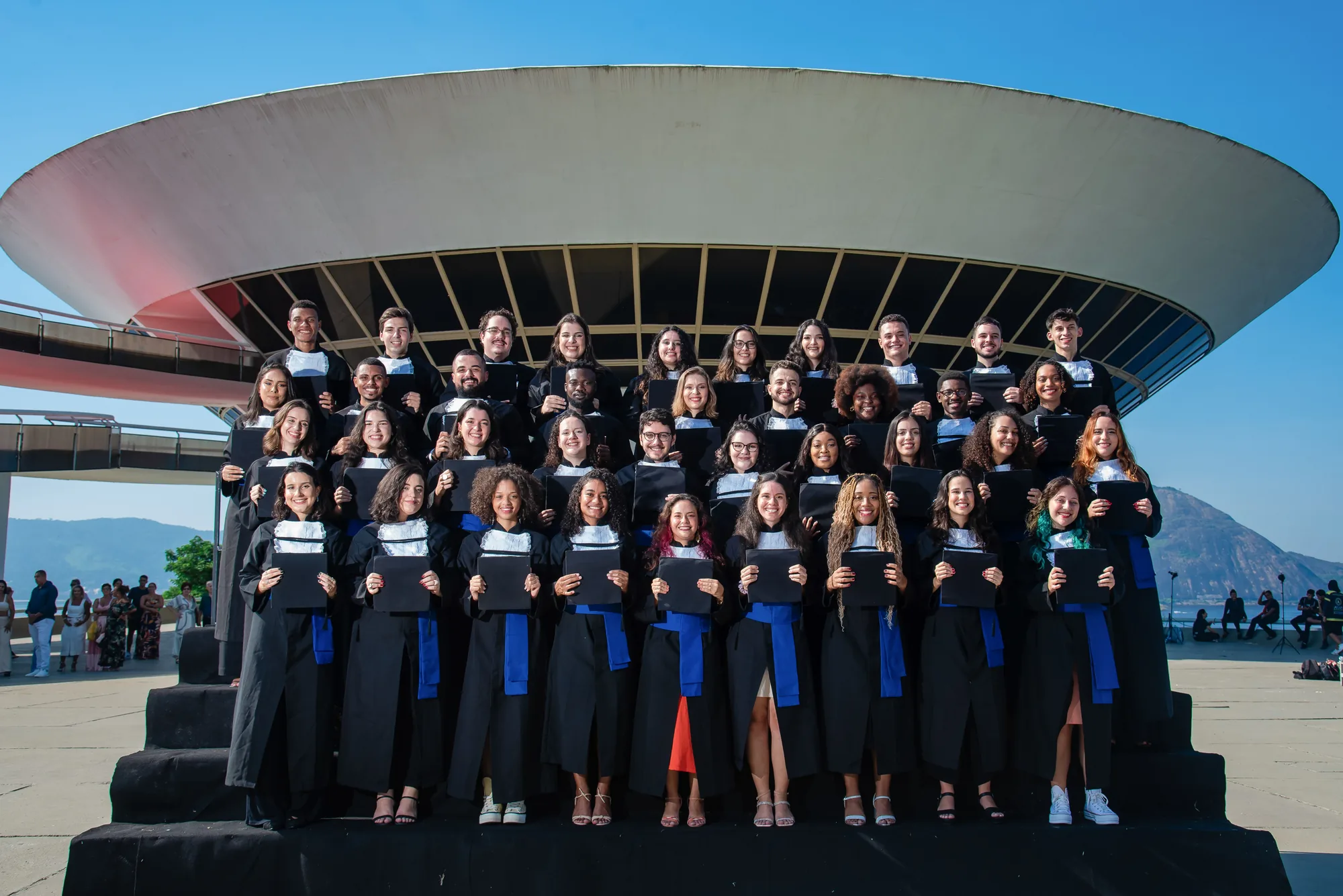 Turma de formandos de beca reunida na escadaria diante do MAC de Niterói