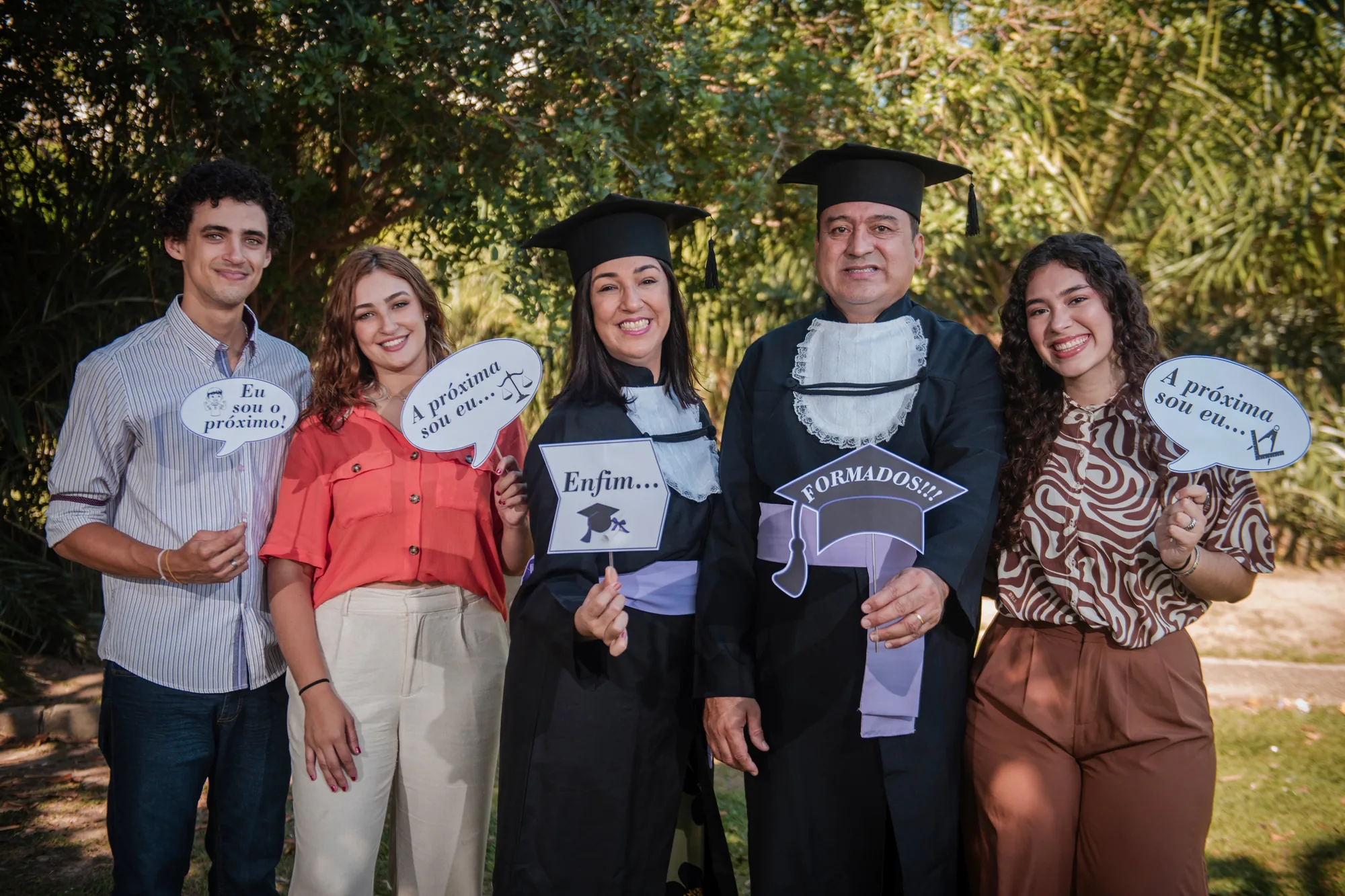 Formandos de beca com a família segurando plaquinhas nos jardins do MAM