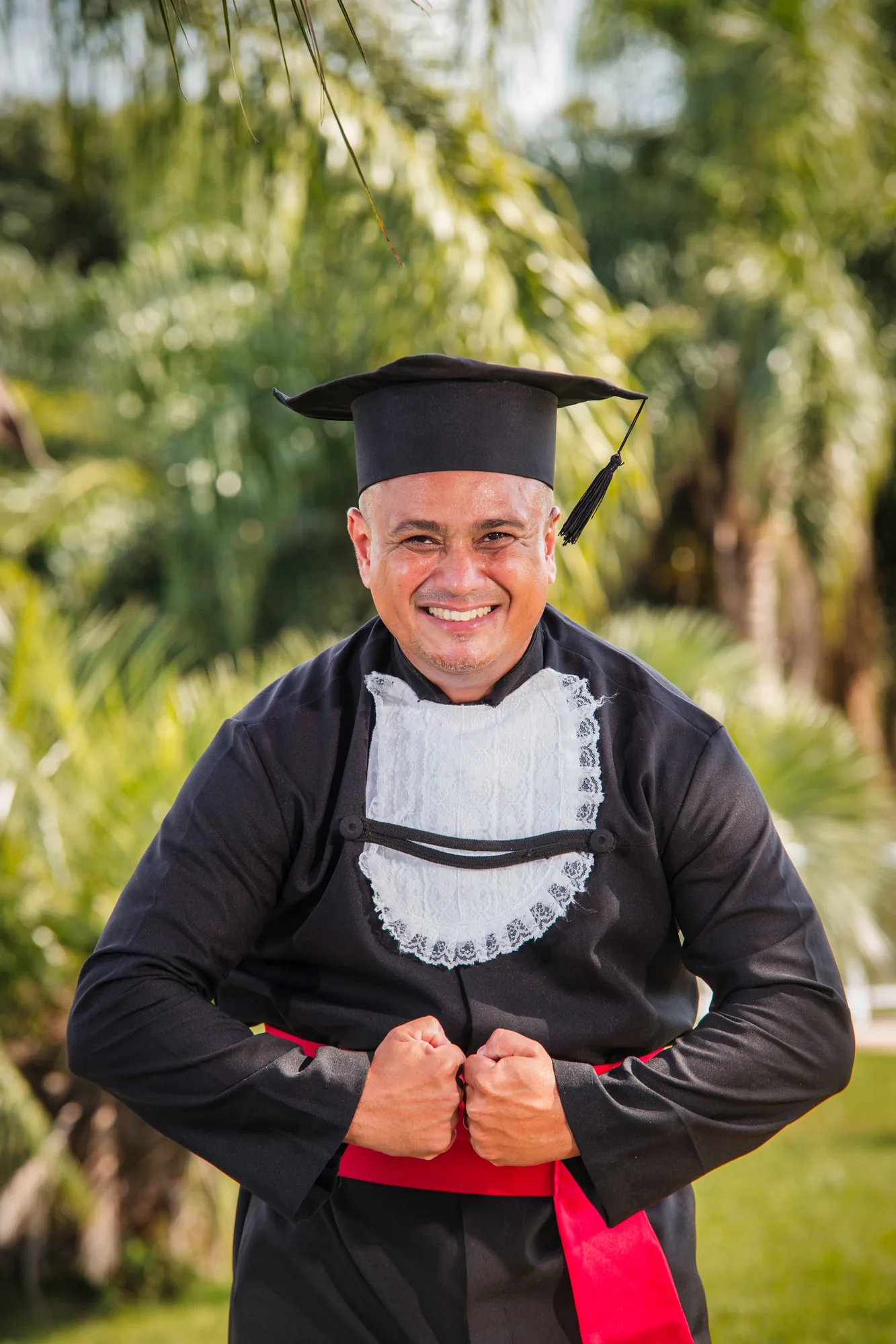 Formando de beca sorri no jardim em Rio das Ostras
