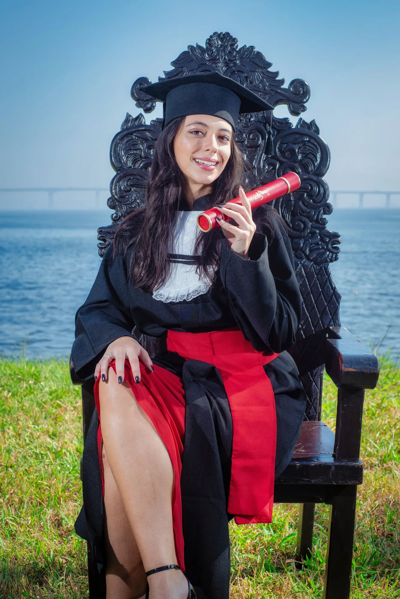 Formanda de beca na cadeira entalhada no campus do Gragoatá