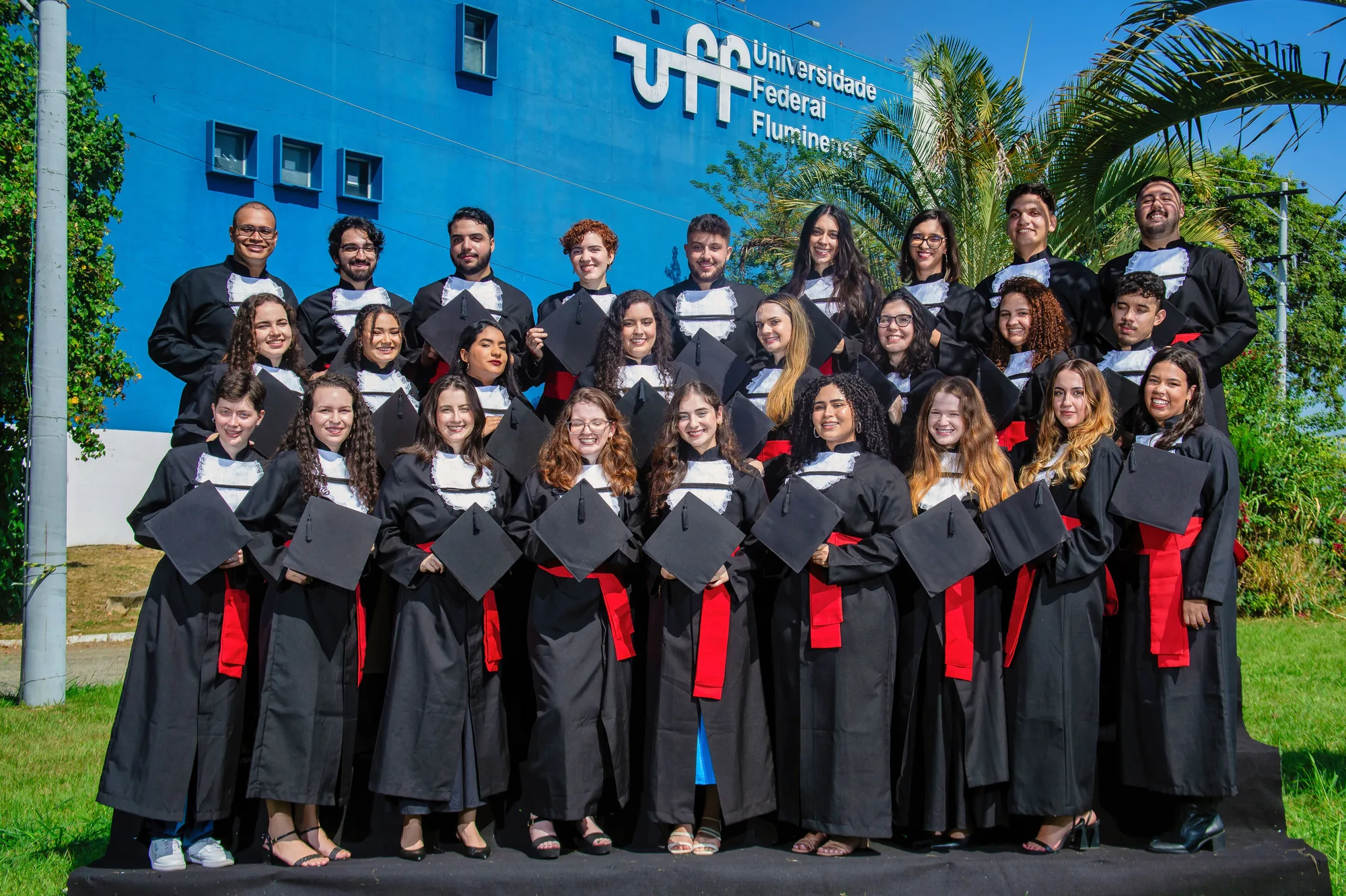 Turma de formandos de beca reunida diante do prédio da UFF, no Gragoatá
