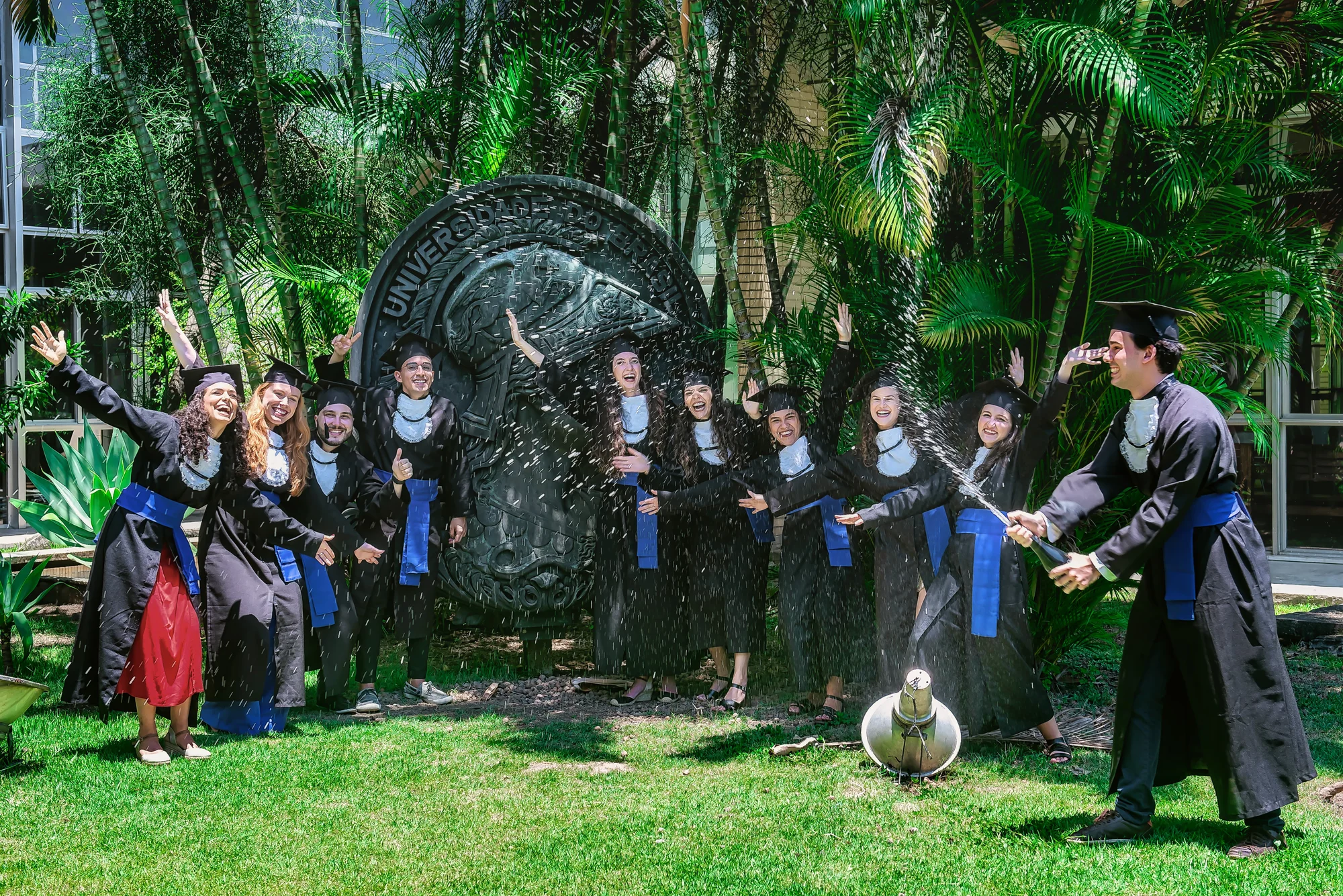 Turma de formandos estoura espumante diante da escultura no campus da UFRJ