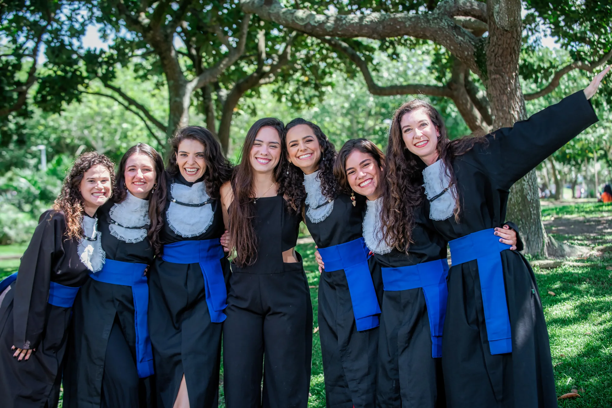 Grupo de formandas de beca abraçadas sob as árvores da UFRJ