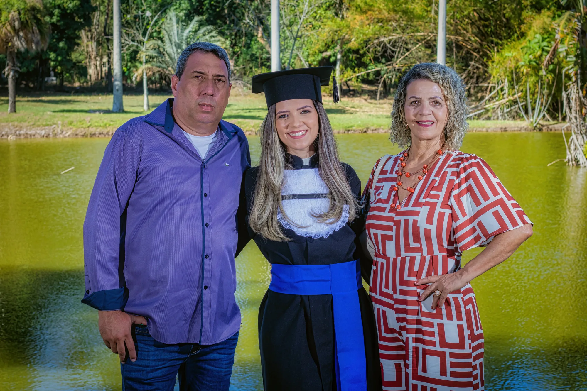 Formanda de beca entre os pais à beira do lago da UFRRJ