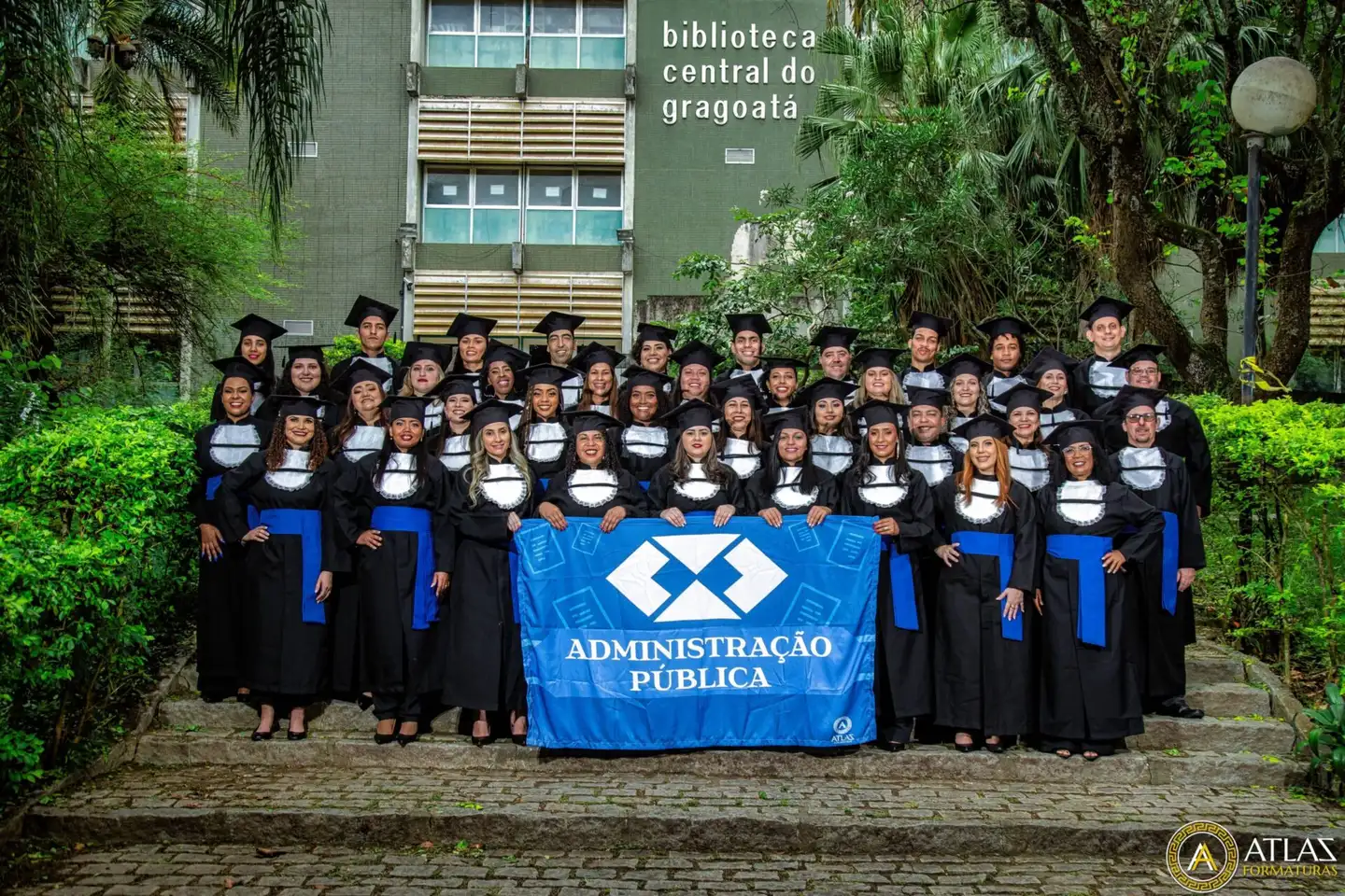 Turma de Administração Pública reunida com a bandeira do curso diante da biblioteca do campus