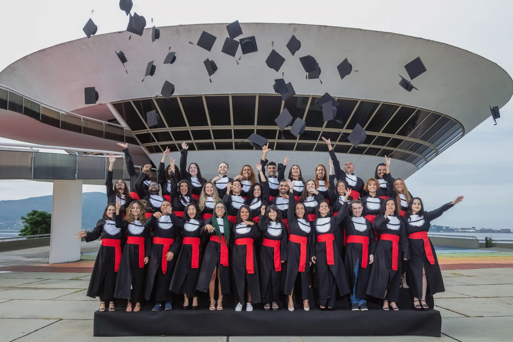 Turma de formandos de beca joga os capelos para o alto diante do MAC de Niterói